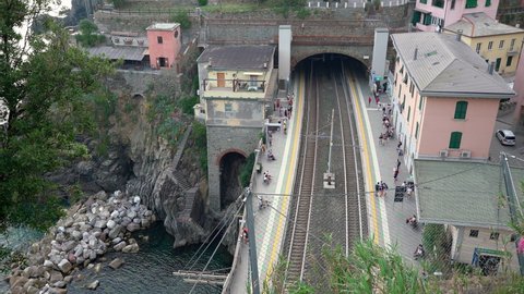 Riomaggiore, Italy - June 11. 2021: Trenitalia Passenger Train enters Train Station in Riomaggiore, Cinque Terre. People leaving Passenger Train seen from above, Aerial view