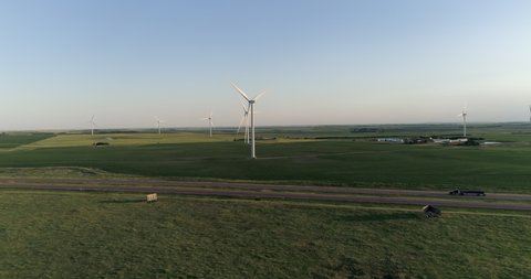 Flying above green meadows towards highway and white wind turbines. Sunset warm sky, South Dakota