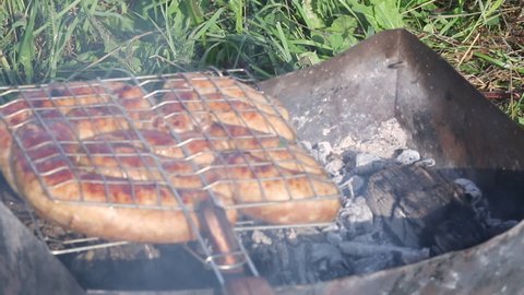 Grill rack with browned sausages. Lies on the grill with embers. In the meadow among the green grass. Picnic in nature. Close-up shot