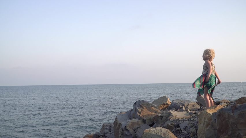 Child girl 4 years old throws stones on the seashore or ocean