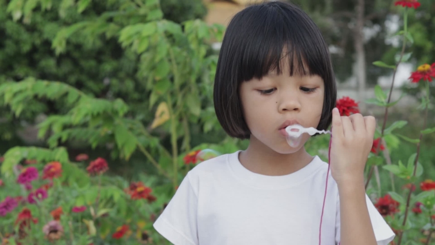 Cute Asian Thai kid girl playing soap bubbles being outside outdoors She had fun blowing bubbles and smiling. Playing outside is learning to enhance children