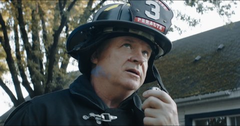 Firefighter chief talking on CB radio and giving orders to his crew, fireman fighting house fire in a neighborhood. Shot with 2x anamorphic lens