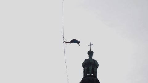 A man fail falls from a slackline hanging from a safety rope silhouette in a sky