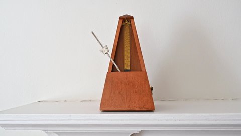 An old fashioned metronome beating at an Adagio pace on a white shelf.