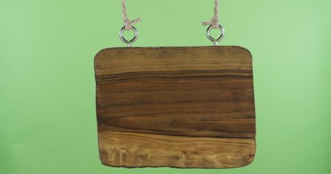 Wooden blank sign hanging from ropes and swinging. Close-up. Isolated on a green background.