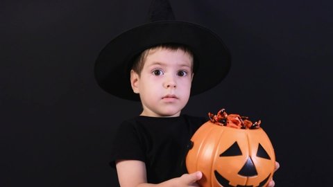 Halloween child. A boy in a sorcerer's costume shows a pumpkin bucket of candies sweets and prepares for the holiday.