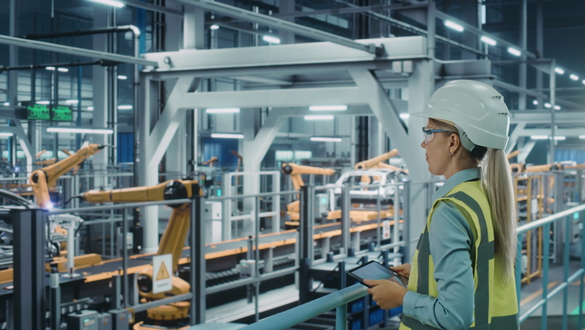 Car Factory: Female Automotive Engineer Using Augmented Reality Tablet Computer. Digitalization Scan, Monitoring Equipment Production. Automated Robot Arm Assembly Line Manufacturing Electric Vehicles