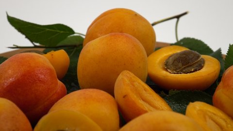 Ripe whole apricots and apricot halves with kernels inside lie on the green leaves of an apricot tree against a white background