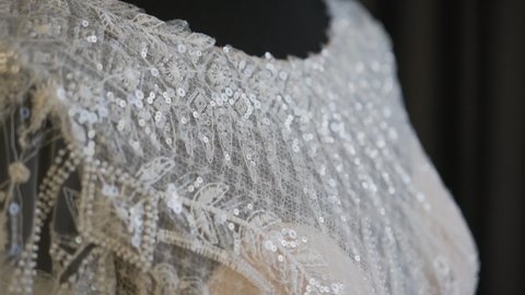The wedding dress lies on a black mannequin. Expensive wedding clothes for the bride made of lace fabric embroidered with shiny round tinsel, shimmering in the light.