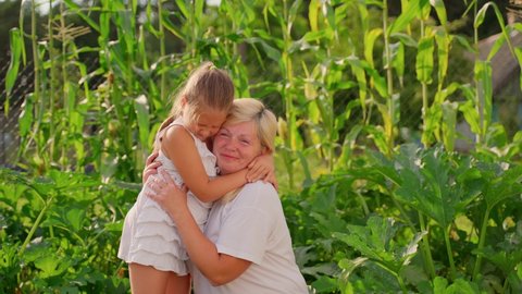 Portrait grandmother and granddaughter hugging in garden outdoors. Two females different generations smile spend time together. Happy family at ranch or farm house concept