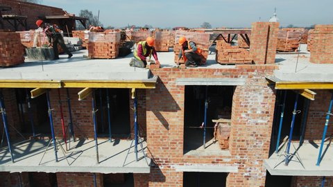 Workers on the construction of a house laying red bricks. Builders are building a brick wall of a high-rise building.
