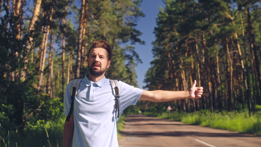 Unhappy young man making hitchhiker gesture, tired of walking long distance