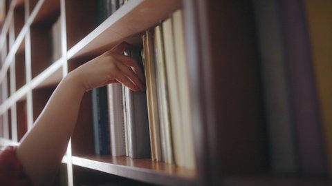 Female librarian looking for book on the bookshelf, student doing research