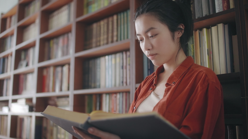 Attractive asian woman librarian flipping through pages of large book at library Royalty-Free Stock Footage #1077640748