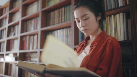 Attractive asian woman librarian flipping through pages of large book at library