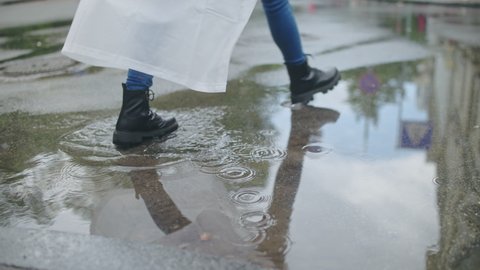 Female in boots and raincoat confidently walking through puddles, big city life
