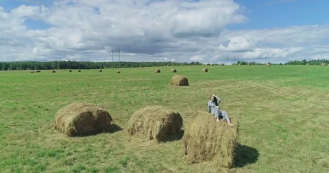 Young stylish girl in suit with animal print sitting on a haystack. Beautiful young girl in the field. Girl looks into the distance. Girl in the countryside. Aerial view, 4k