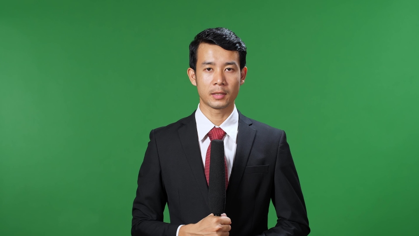 Asian Male Tv News Reporter In Formal Wear Talking On A Green Screen, Chroma Key
