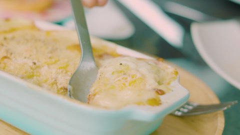 Close up and selective focus of fresh cooked gratin which is french cuisine of macaroni baked with parmesan cheese was served on table, and seeing people hand using spoon scoop it.