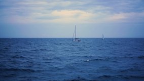 A sailing catamaran yacht floats on the waves in the sea against the background of yachts. Russia. Summer cloudy evening, dark sky with clouds, seascape, 4k