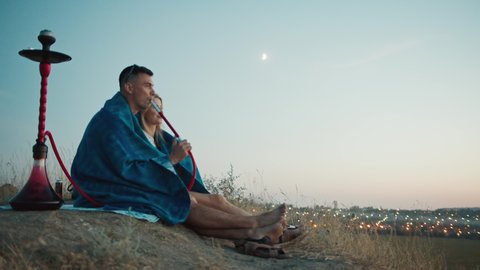 a guy and a girl enjoy the sunset and a view of the city, smoke a hookah, sit in an embrace, enjoying the view of the city.