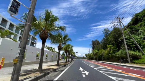 OKINAWA, JAPAN - JUNE 2021 : Driving shot of Okinawa. Wide camera, point of view, seaside road driving. Blue sunny summer sky. Relaxing holiday, vacation and adventure journey travel concept shot.