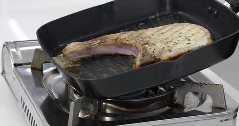 Pork steak cooking in black pan with smoke from hot on gas stove.