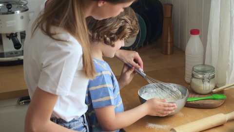 Family cooking in kitchen. Mother teaches son to make dough stir ingredients with whisk