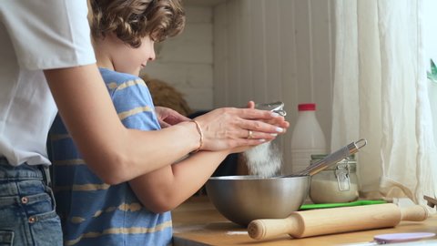 Mom and son cook in kitchen woman helps child to sieve flour