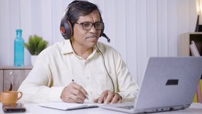 Middled aged Businessman with headphones attending online and making notes glass from office - concept of never stop learning and business training.