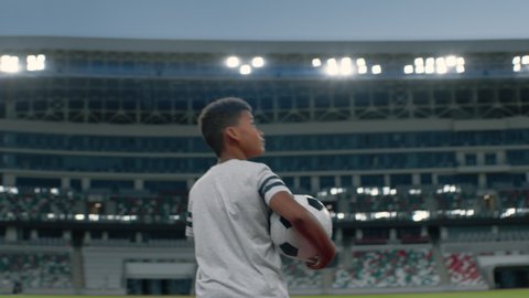 Portrait of African American Black dreamer kid boy walking onto the field of huge soccer football stadium, holding a ball, dreaming of becoming professional player, soccer star