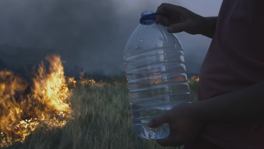 A volunteer man or boy extinguishes a wild fire. Pours water from a plastic bottle. Rain forest wildfire disaster, dry bushes burning, fire reasons, ecology, earth, climate change, air pollution Royalty-Free Stock Footage #1077683615
