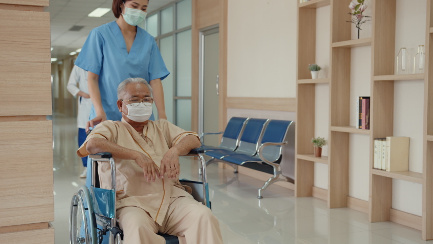 Young Asian woman nurse caregiver wear medical face mask encourage take care her patient explain information use wheelchair in hospital ward, Epidemic and virus, Hospital environment concept.