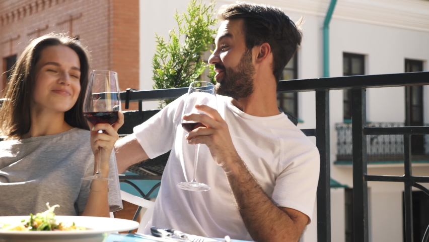Smiling beautiful woman and her handsome boyfriend. Happy cheerful family. Couple cheering with glasses of red wine at their date in restaurant. They drinking alcohol at veranda cafe in the street Royalty-Free Stock Footage #1077695612