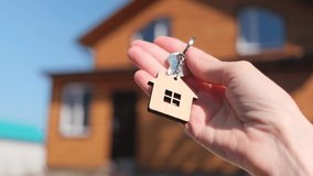 Close-up of a key with a house-shaped keychain in hand. In the background is a house. The concept of buying and insuring real estate, cottage, mortgage. Copy space. - Powered by Shutterstock - Get 15% off with code: PIKWIZARD15