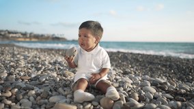 Charming Asian little boy playing with rocks on Mediterranean sea coast with azure turquoise waves rolling on beach at background in slow motion. Portrait of cute child on rocky coastline at sunset - Powered by Shutterstock - Get 15% off with code: PIKWIZARD15