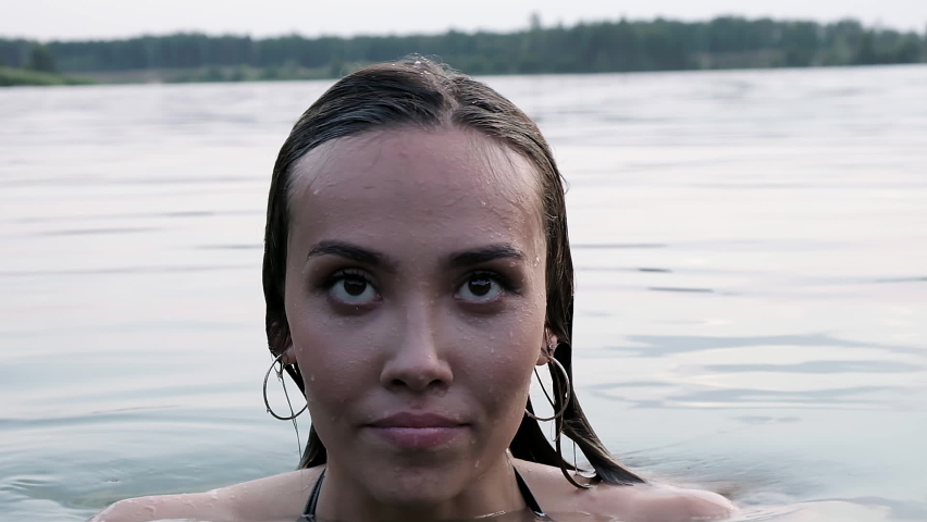 closeup on sexy seductive young woman who swims in lake, staying in water. attractive asian fit female with long hair in swimsuit swimming in pond. summer chill, vacation, rest, relaxing at nature