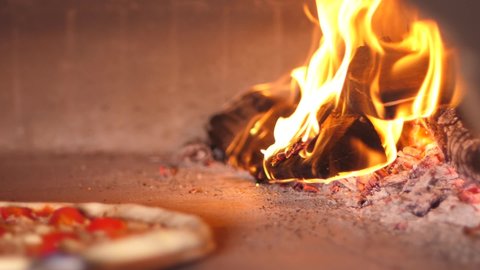 Baking pizza in the oven in pizzeria near open fire of burning wood