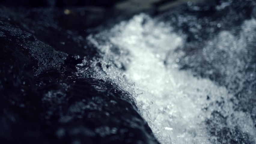A wild mountain river with crystal clear water. Well water is flowing over stones. Abundant clear stream in a forest. Cold water splashing near rapids. Concept of water background. Slow motion shot.