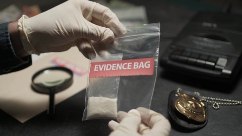 Police officer is investigating an evidence bag with cocaine powder inside at his desk