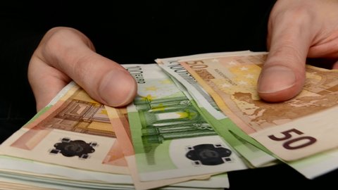 Ungraded: Counting euros. A man counts a bundle of 50 and 100 Euro banknotes. Close-up of hands on black backgound. Ungraded H.264 from camera without re-encoding.