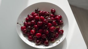 Plate with fresh red cherries on the table in the room on a summer sunny day. High quality 4k footage