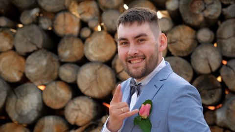 Beard groom show gesture goat. Symbol horn rock on fingers arm wedding man. Looking at camera on wood background. People in suit showing sign rock n roll. Groom in wedding bow tie gesturing hand goat.