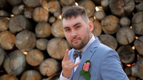 Beard groom show gesture goat. Symbol horn rock on fingers arm wedding man. Looking at camera on wood background. People in suit showing sign rock n roll. Groom in wedding bow tie gesturing hand goat.