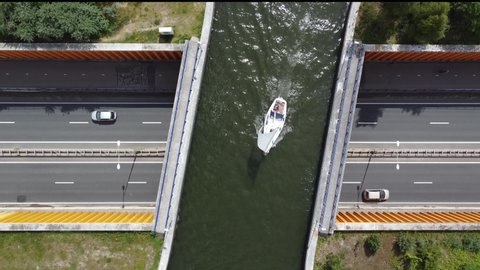 Aerial view of modern aqueduct or water bridge is constructed to convey watercourses across gaps showing a sailboat moving over the infrastructure and vehicles cars driving under 4k high resolution