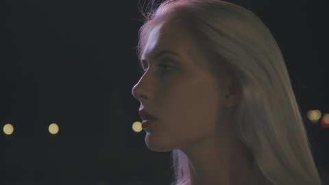 A portrait in profile of a young woman against the background of the lights of the night city. Slow motion. Closeup