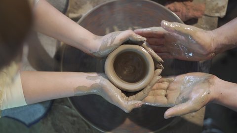 An expert potter, he teaches his student to make a clay bowl and passes on the ancient tradition of creating works of art from generation to generation. Concepts of: art, tradition, family. Top view.