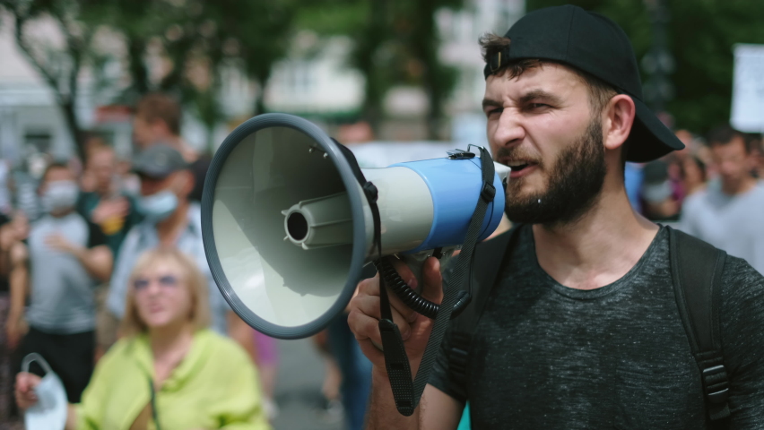 Angry political protester guy with bullhorn marches in protest crowd. Male rebel speaking on demonstration revolt resistance. Strike activist demonstrator man on opposition rally riot with megaphone. Royalty-Free Stock Footage #1077722375