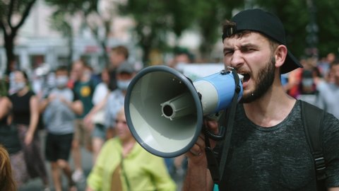 Angry political protester guy with bullhorn marches in protest crowd. Male rebel speaking on demonstration revolt resistance. Strike activist demonstrator man on opposition rally riot with megaphone.