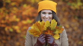 Hello october. smiling elegant woman in brown coat and yellow hat with autumn yellow leaves outdoors in the city park in autumn. This video was made with PRORes 422 codec.